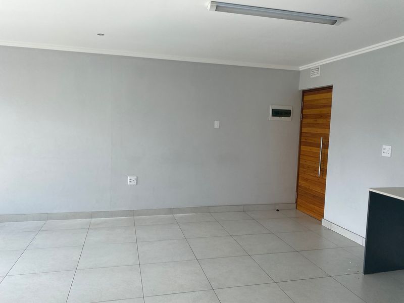 A bright, empty open-plan living area featuring neutral tiled flooring, a modern wooden door, and clean wall finishes.