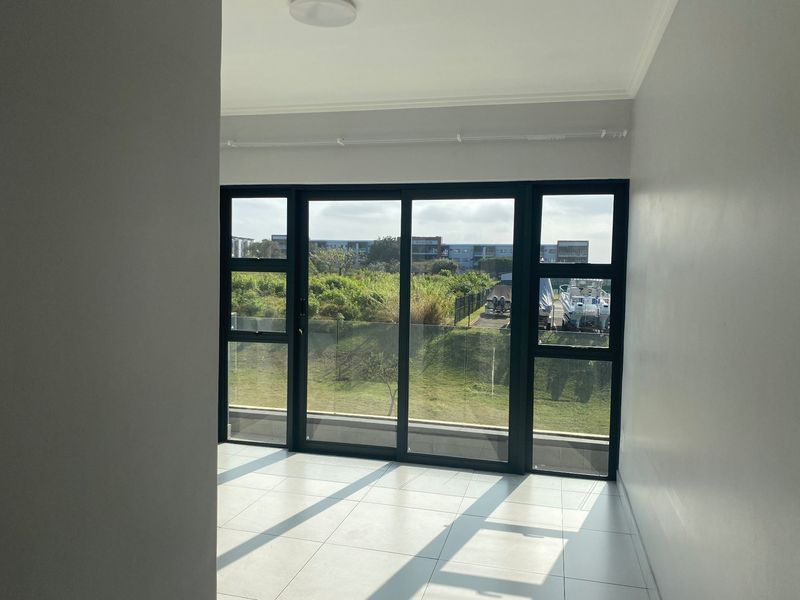 A bright, empty living area featuring large sliding glass doors that open to a balcony with a glass balustrade and scenic outdoor views.