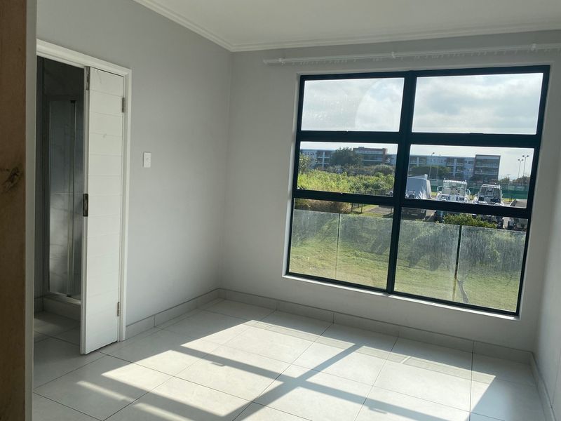 A bright, empty bedroom featuring neutral tiled flooring, large windows with natural light, and direct access to an en-suite bathroom.