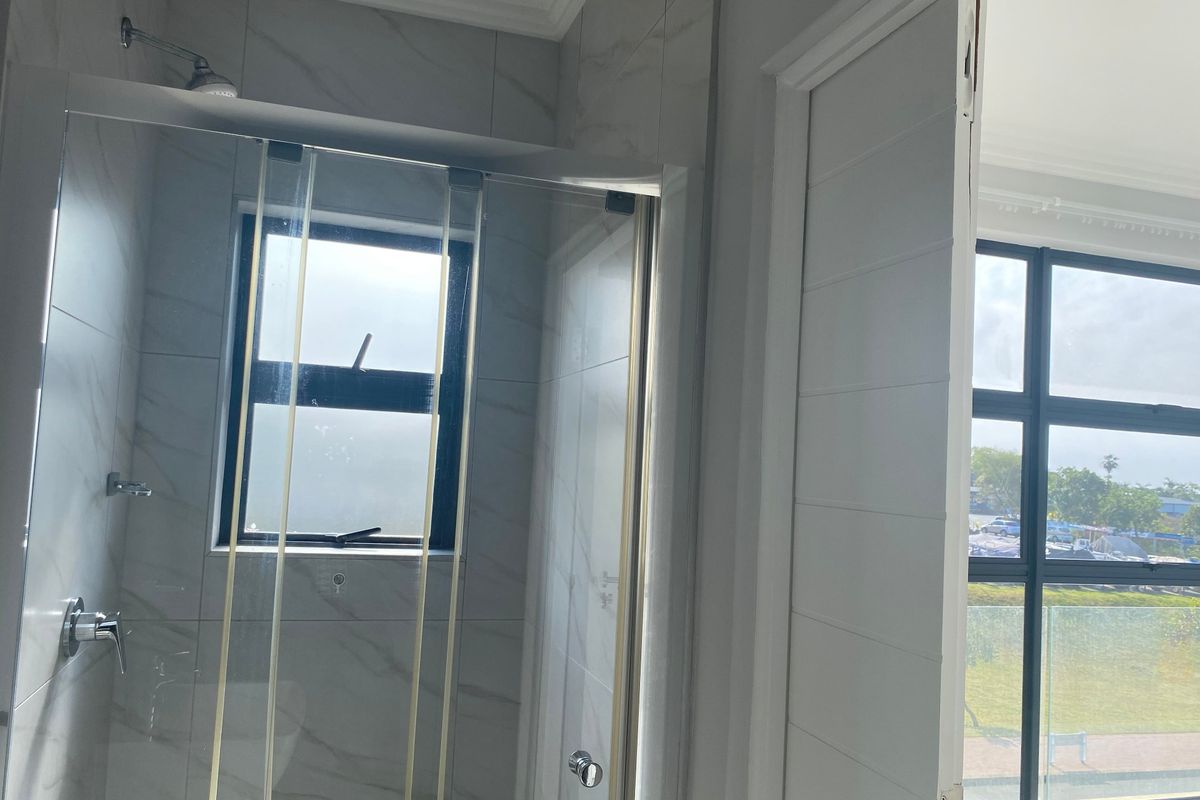 A modern bathroom featuring a glass-enclosed shower with marble-look wall tiles and large windows providing natural light.