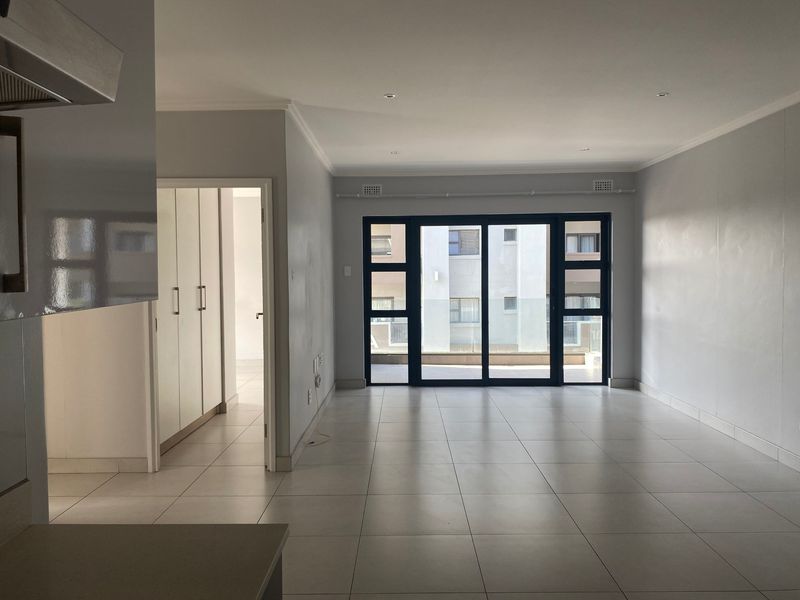Spacious open-plan living area featuring neutral tiled flooring, recessed lighting, and large sliding glass doors leading to an outdoor balcony.