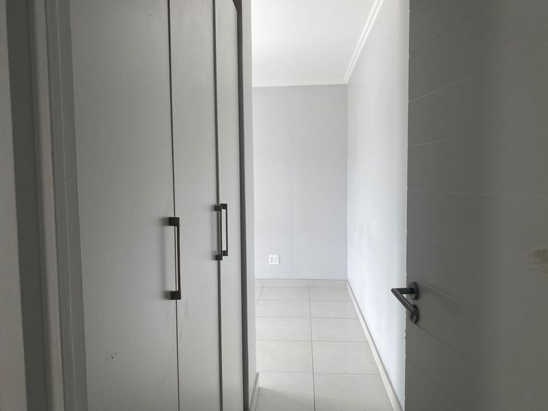 A clean, empty hallway featuring neutral tiled flooring and built-in cupboards with modern hardware.