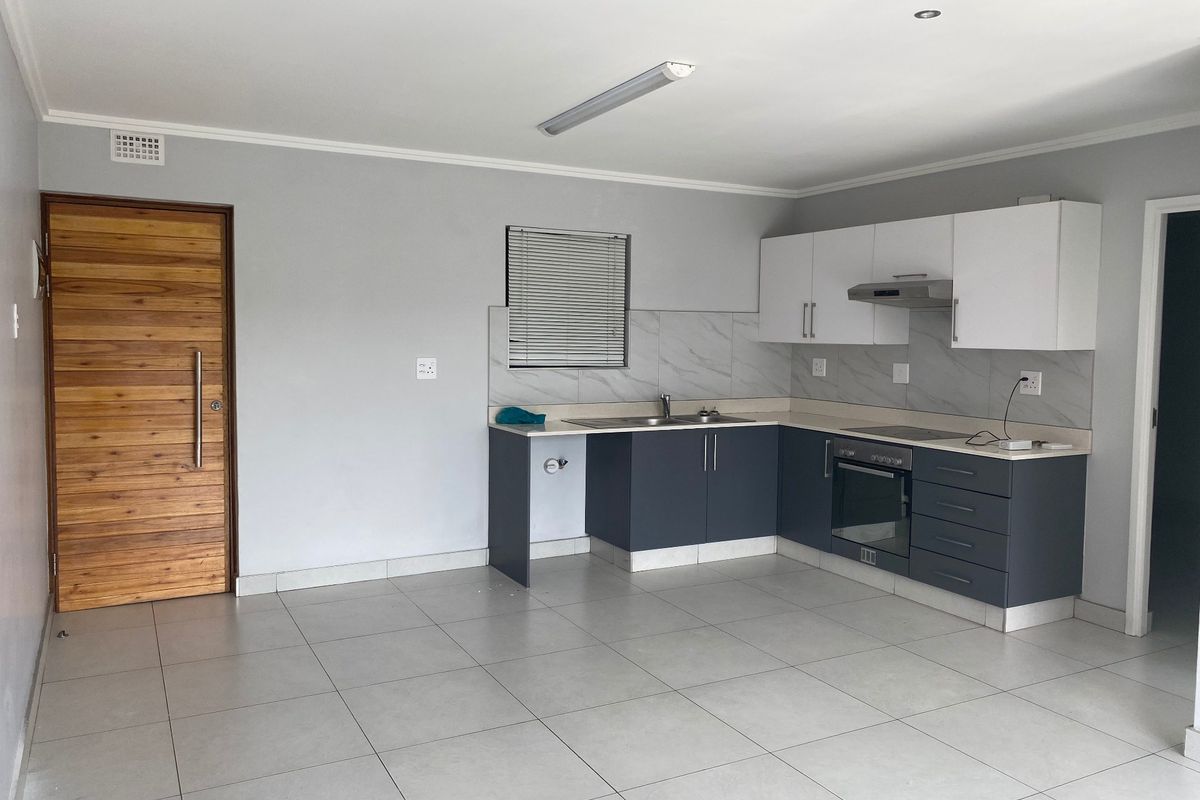 A clean, modern kitchen featuring two-tone cabinetry, built-in oven, extractor fan, and neutral tiled flooring in an open-plan layout.