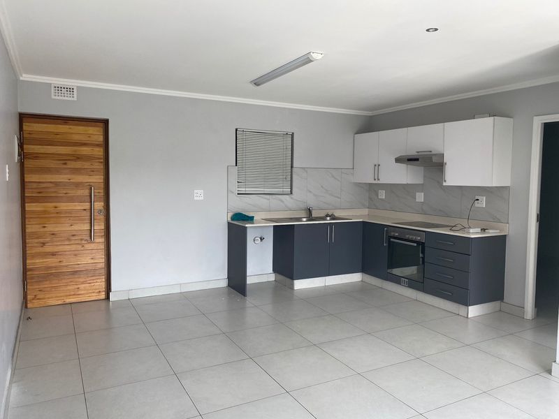 A clean, modern kitchen featuring two-tone cabinetry, built-in oven, extractor fan, and neutral tiled flooring in an open-plan layout.