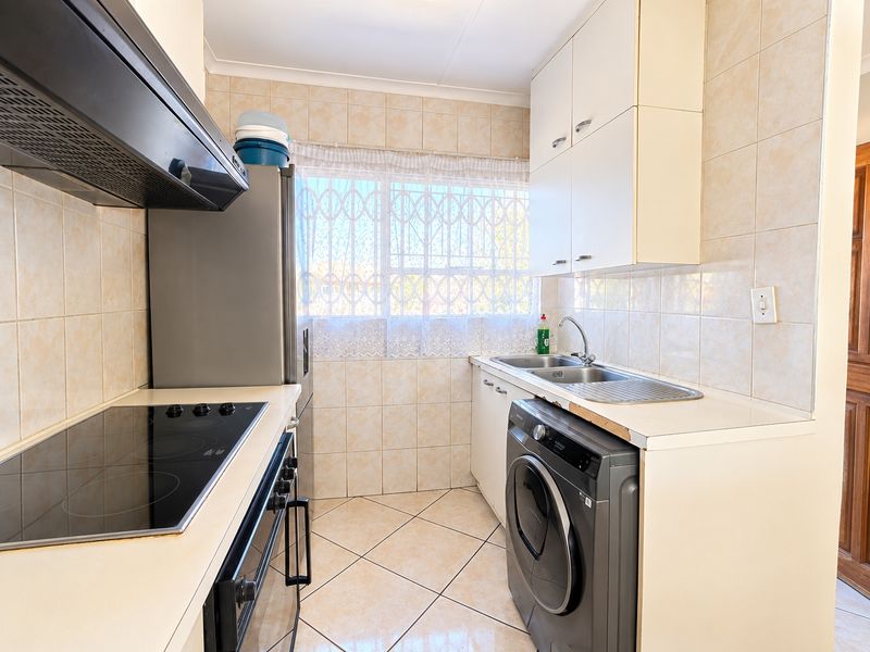 Functional kitchen featuring built-in cabinetry, electric hob, oven, extractor fan, and stainless steel sink with tiled finishes throughout.