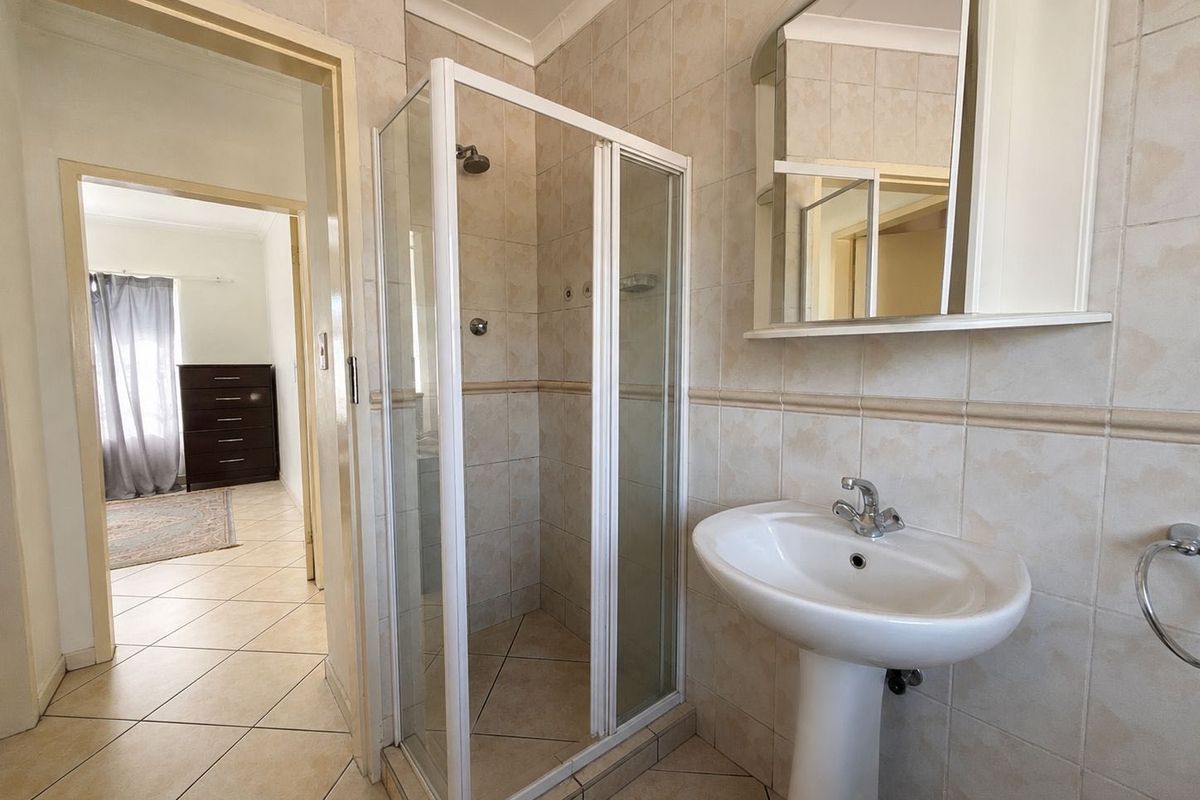 A functional bathroom featuring a pedestal basin, a shower enclosure with glass doors, and neutral wall and floor tiling.