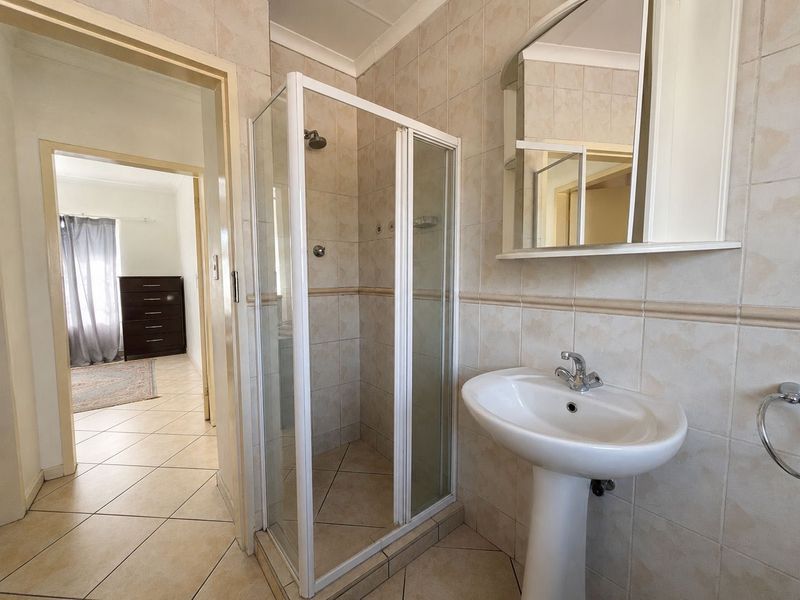A functional bathroom featuring a pedestal basin, a shower enclosure with glass doors, and neutral wall and floor tiling.