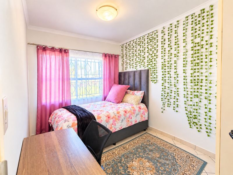 A well-lit bedroom featuring tiled flooring, a window with security bars, and a neutral interior finish.