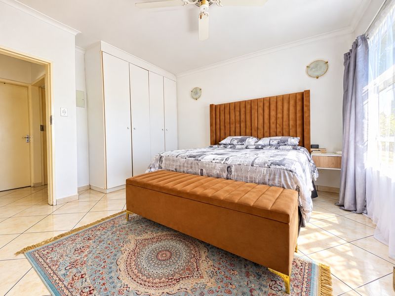 A well-maintained bedroom featuring tiled flooring, built-in cupboards, a ceiling fan, and wall-mounted lighting.