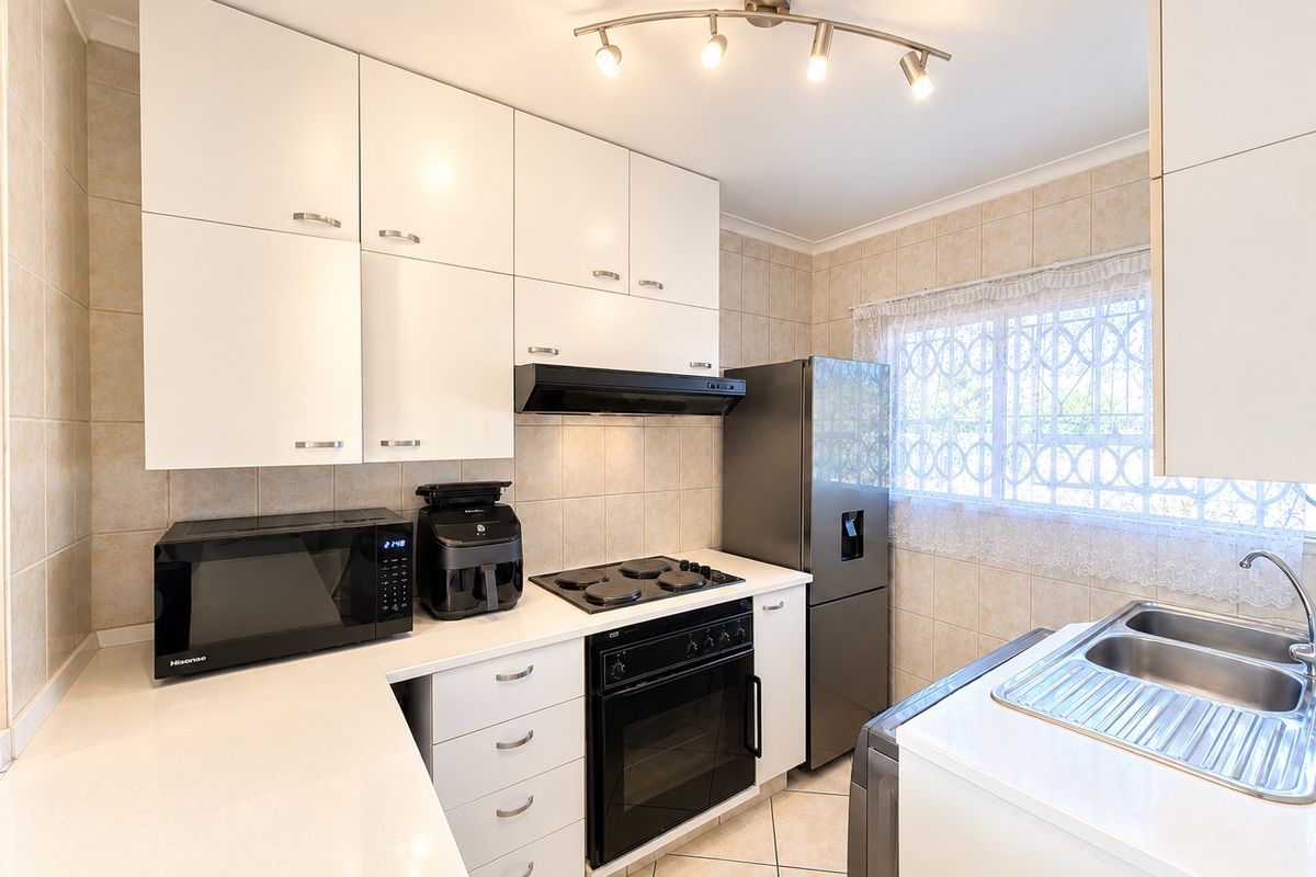 A functional kitchen featuring white cabinetry, built-in oven with electric hob, extractor fan, and a double stainless steel sink with tiled finishes.