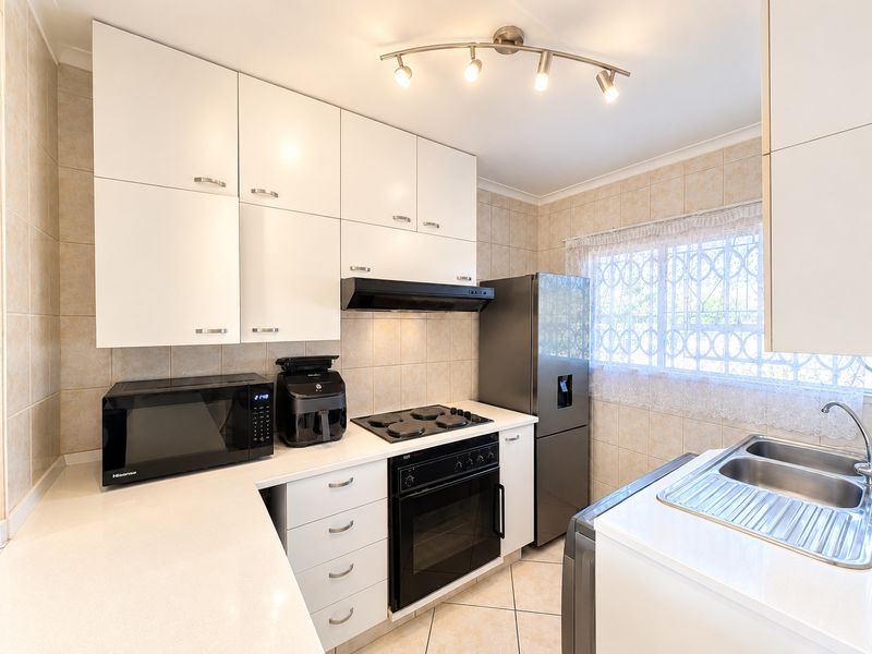 A functional kitchen featuring white cabinetry, built-in oven with electric hob, extractor fan, and a double stainless steel sink with tiled finishes.