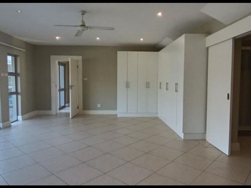 Spacious bedroom featuring neutral tiled flooring, extensive built-in cupboards, a ceiling fan, and direct access to an outdoor patio area.