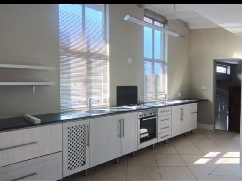 A clean, modern kitchen featuring light-toned cabinetry, dark stone countertops, built-in oven, and large windows providing ample natural light.