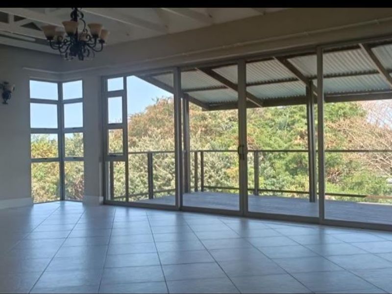 Spacious living area featuring tiled floors, exposed beam ceilings, and large sliding glass doors opening onto a private balcony with scenic views.