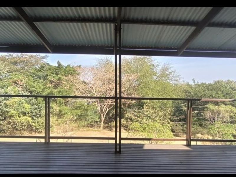 A spacious covered timber deck featuring a corrugated metal roof, steel support posts, and wire balustrade, offering elevated views of the surrounding trees.