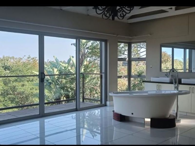 Spacious modern bathroom featuring a freestanding bathtub, double vanity, and large sliding glass doors opening onto a private deck with scenic views.