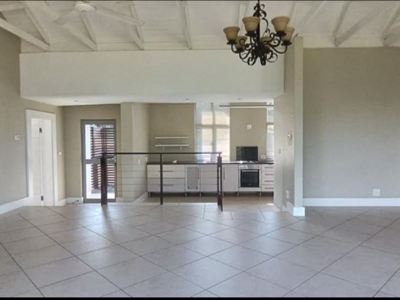 Spacious open-plan living area featuring vaulted ceilings with exposed rafters, tiled flooring, and an integrated kitchen with built-in cabinetry and appliances.