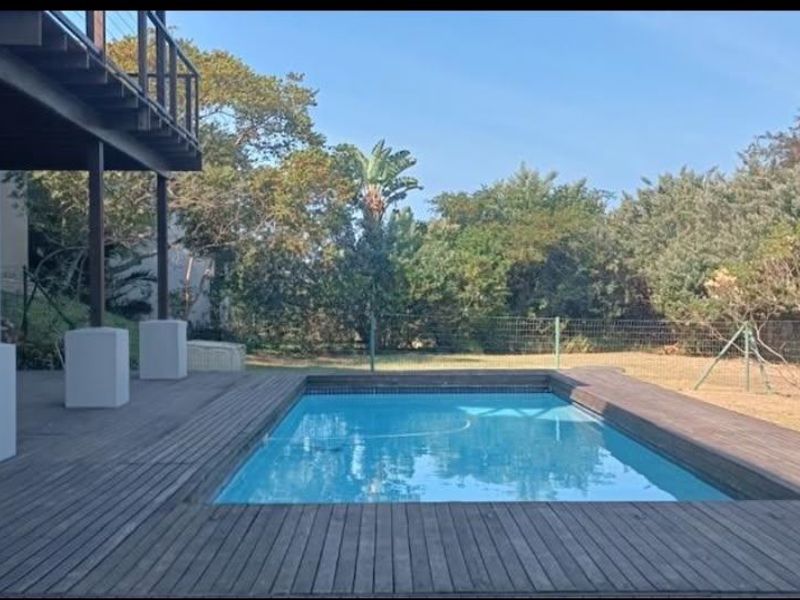 Outdoor pool area featuring timber decking, a covered patio space, and a private garden setting with established trees.