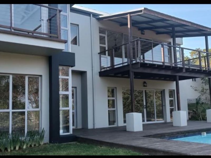 Rear elevation of a modern double-story home featuring a swimming pool, wooden decking, and a spacious covered balcony with glass balustrades.