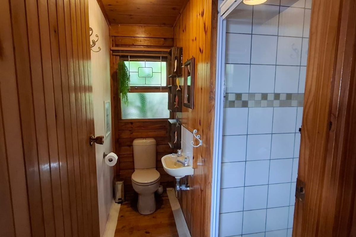 Compact bathroom featuring timber wall paneling, wooden flooring, a wall-mounted basin, and a separate shower enclosure with tiled walls.