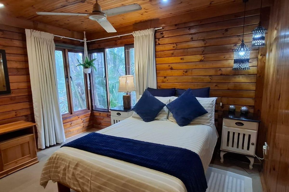A cozy bedroom featuring warm timber wall paneling, a timber ceiling with a built-in fan, and large windows allowing natural light.