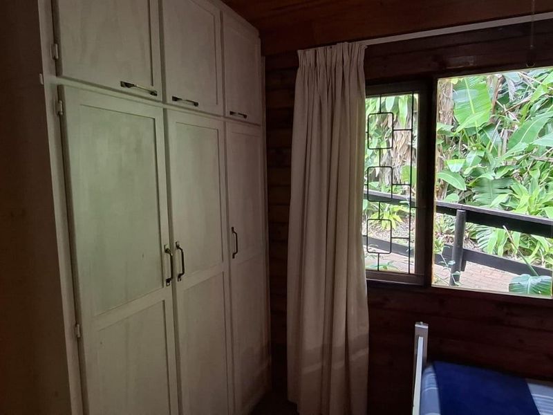 Bedroom featuring built-in cupboards and timber wall paneling, with large windows overlooking a lush garden area.