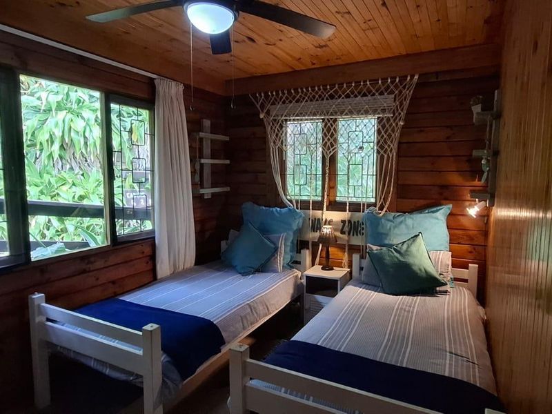 A cozy bedroom featuring warm timber wall and ceiling cladding, a ceiling fan, and windows fitted with security bars.