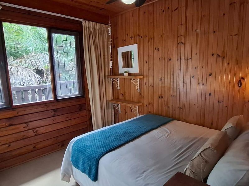 A cozy bedroom featuring warm timber wall paneling, a timber ceiling, and a window with security bars overlooking the exterior.