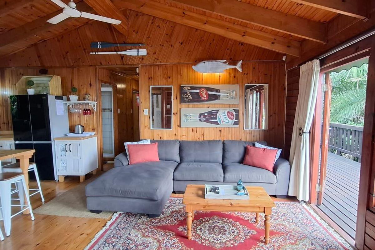 Open-plan living area featuring warm timber-clad walls, exposed ceiling beams, timber flooring, and direct access to an outdoor deck through sliding glass doors.