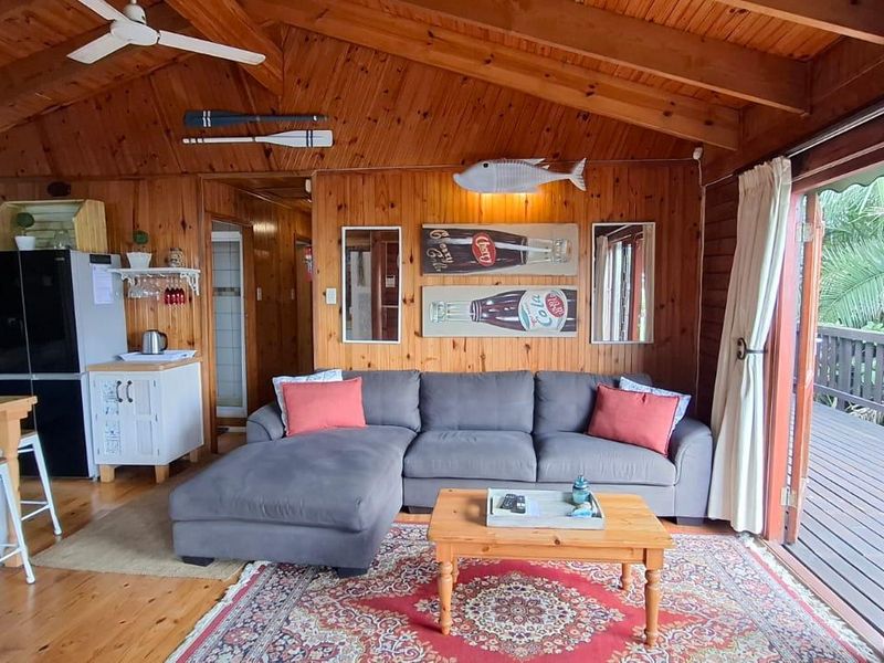 Open-plan living area featuring warm timber-clad walls, exposed ceiling beams, timber flooring, and direct access to an outdoor deck through sliding glass doors.