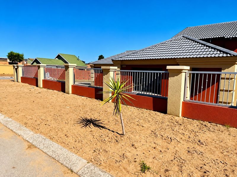 Front exterior view of the property featuring a tiled roof, perimeter wall with metal fencing, and an unlandscaped sandy front yard area.