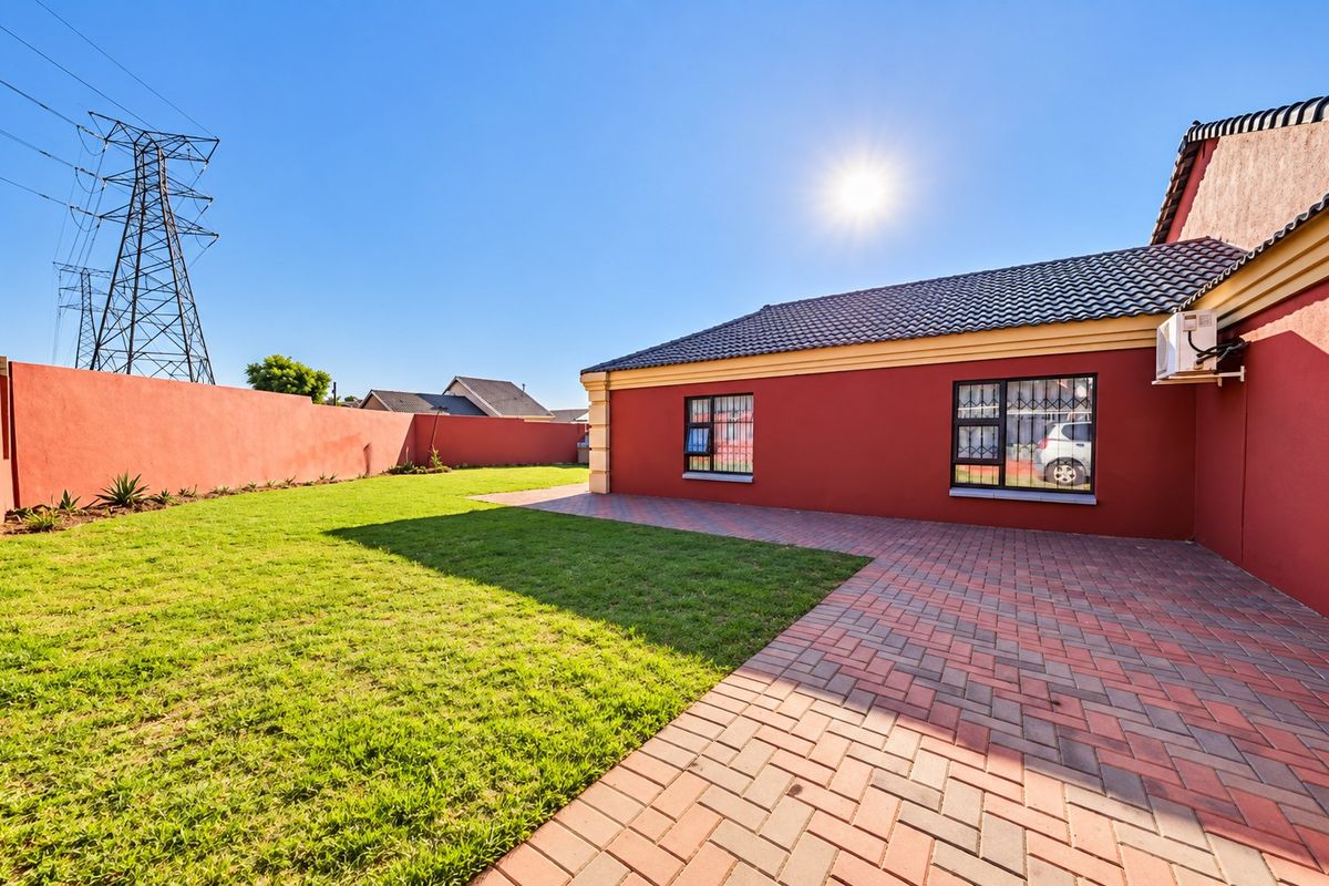 Rear view of the property featuring a paved patio area, well-maintained lawn, and secure boundary walling.
