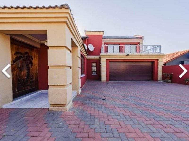 Front elevation of a two-story house featuring a paved driveway, double garage, and a balcony with a decorative wooden entrance door.