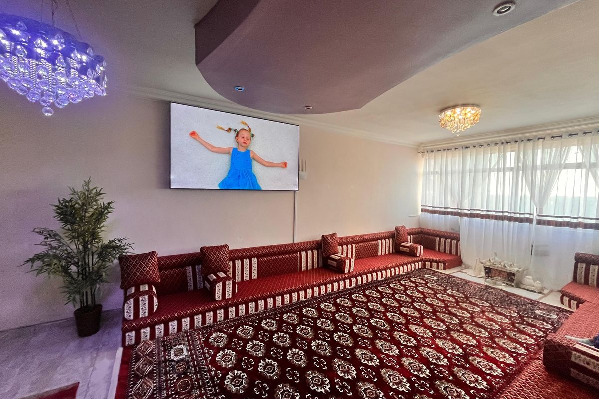 Spacious living room featuring a decorative recessed ceiling, crystal lighting fixtures, and large windows with installed curtain tracks.