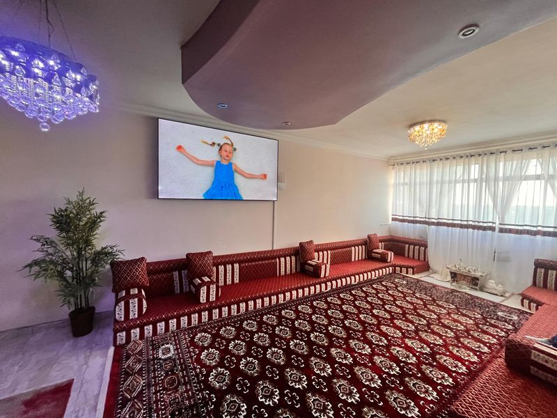 Spacious living room featuring a decorative recessed ceiling, crystal lighting fixtures, and large windows with installed curtain tracks.