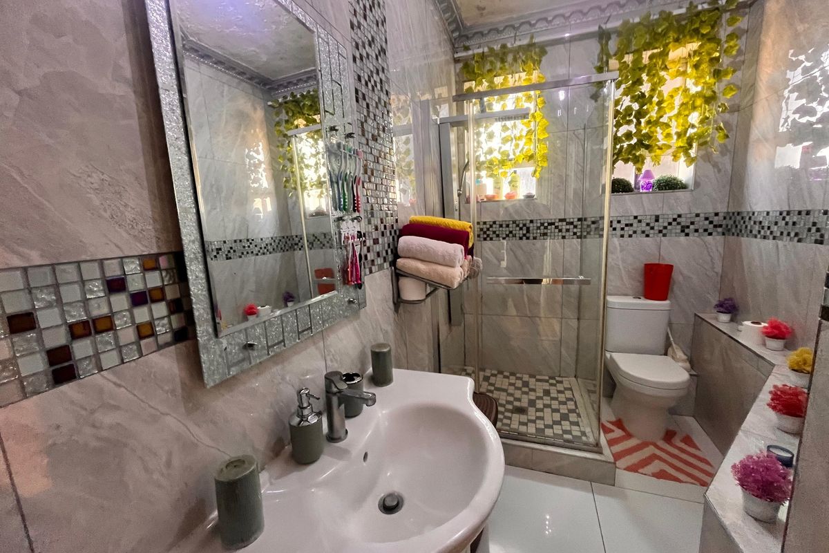 A compact bathroom featuring a pedestal basin, glass-enclosed shower, and decorative mosaic tile accents with neutral wall and floor tiling.