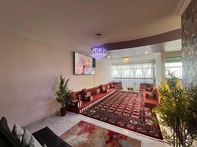 Spacious living area featuring tiled flooring, decorative stone wall accents, and elegant crystal chandelier lighting, creating a warm and inviting atmosphere.