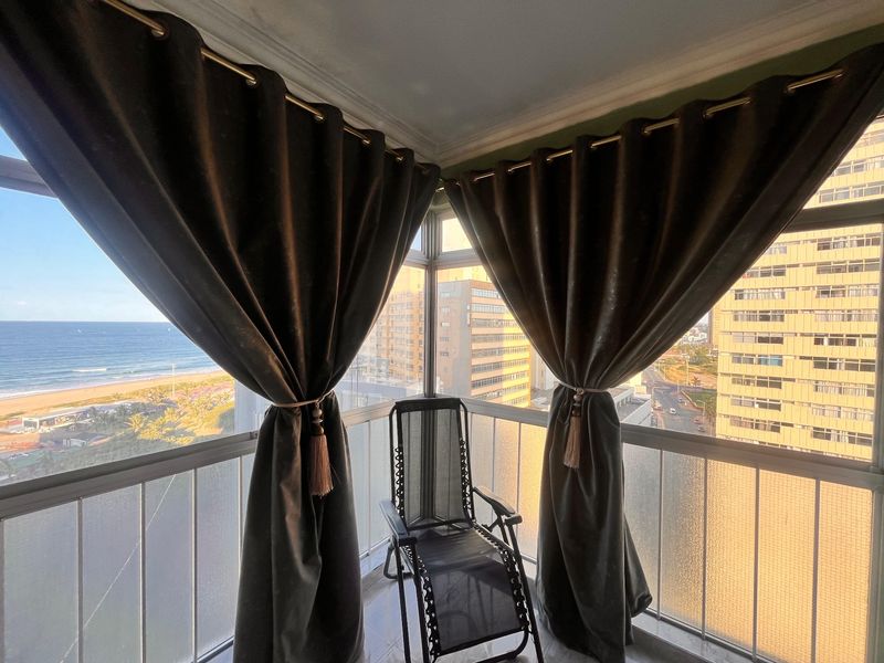 Enclosed balcony featuring tiled flooring and a metal balustrade, offering expansive views of the coastline and surrounding urban landscape.