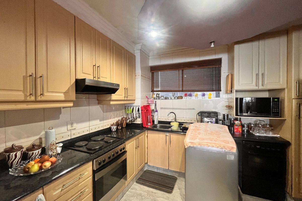 A functional kitchen featuring light wood cabinetry, dark granite countertops, integrated appliances including an oven and hob, and tiled finishes throughout.