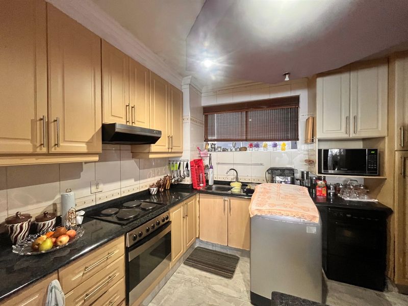 A functional kitchen featuring light wood cabinetry, dark granite countertops, integrated appliances including an oven and hob, and tiled finishes throughout.