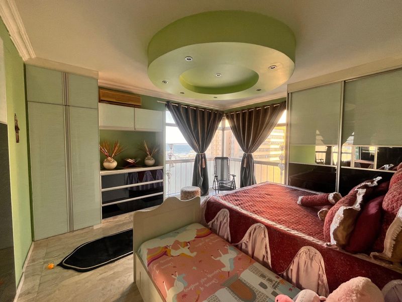 A bedroom featuring built-in cupboards, a unique circular recessed ceiling design, and direct access to a balcony with coastal views.