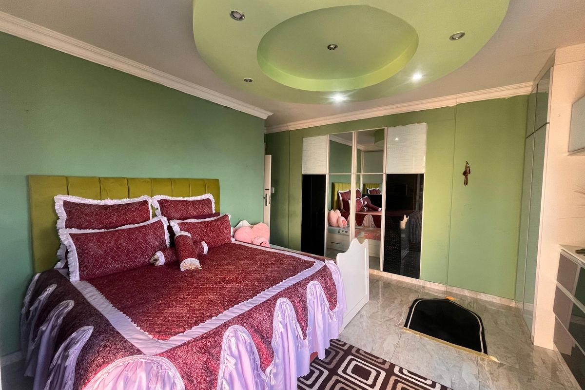 Spacious bedroom featuring a unique circular recessed ceiling design with integrated downlights, tiled flooring, and a large built-in mirrored wardrobe.