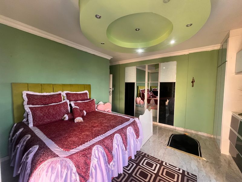 Spacious bedroom featuring a unique circular recessed ceiling design with integrated downlights, tiled flooring, and a large built-in mirrored wardrobe.