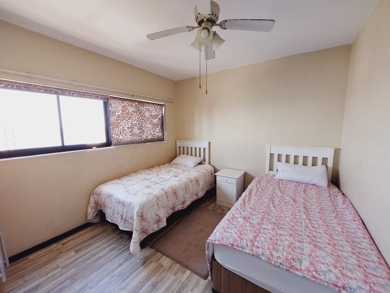 A functional bedroom featuring laminate flooring, a ceiling fan, and a large sliding window providing natural light.