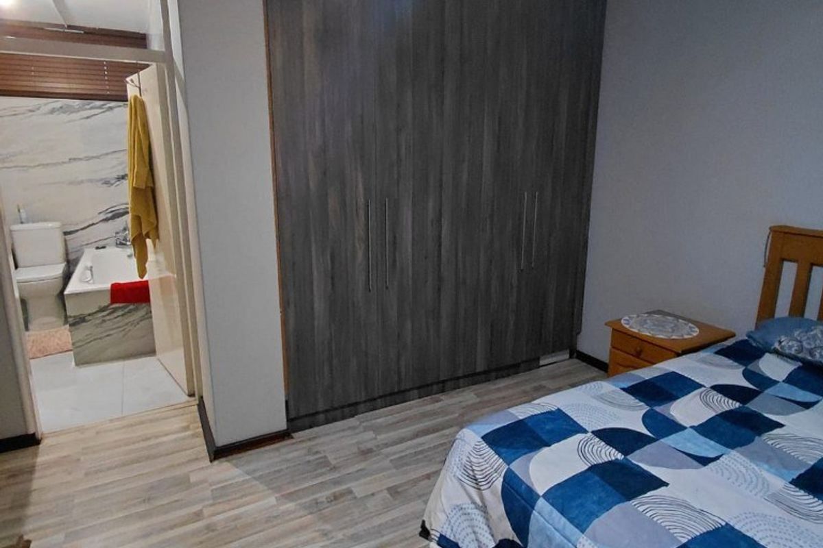A well-maintained bedroom featuring modern laminate flooring, built-in cupboards, a ceiling fan, and direct access to an en-suite bathroom.