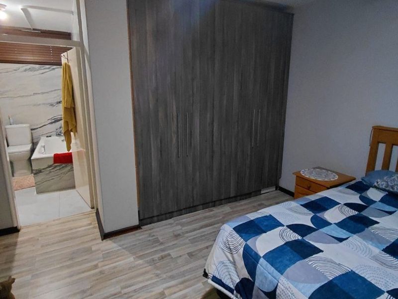 A well-maintained bedroom featuring modern laminate flooring, built-in cupboards, a ceiling fan, and direct access to an en-suite bathroom.