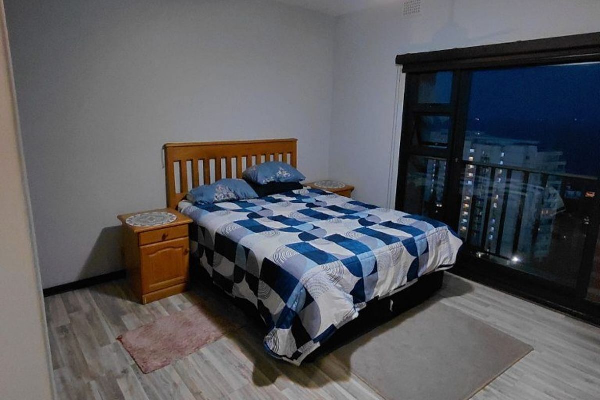 A bedroom featuring laminate flooring, a ceiling fan, and a large sliding glass door providing access to a balcony.