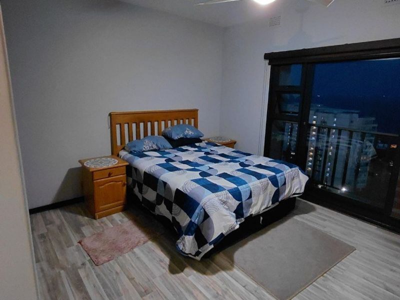 A bedroom featuring laminate flooring, a ceiling fan, and a large sliding glass door providing access to a balcony.
