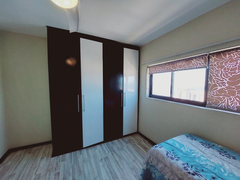 A well-maintained bedroom featuring modern built-in wardrobes with a two-tone finish, laminate flooring, and a sliding window providing natural light.