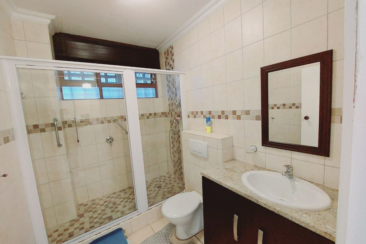 A functional bathroom featuring a walk-in shower with glass enclosure, wall-mounted toilet, and a vanity cabinet with a granite countertop.
